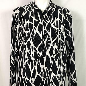 May include: Black and white patterned button-down shirt. The long-sleeved shirt features a bold, abstract design with irregular shapes and dotted accents. The shirt is displayed on a mannequin against a white background.