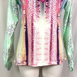 Op de afbeelding: Een shirt met lange mouwen met een kleurrijke, abstracte print. Het shirt heeft een lichtgroene achtergrond met een roze, gele en blauwe print.