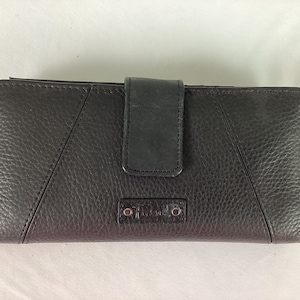 May include: Black leather wallet with a textured finish and a flap closure. The wallet has a silver metal logo that reads "Fossil".