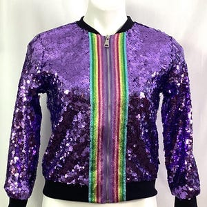 May include: A purple sequined bomber jacket with a rainbow stripe down the front zipper. The jacket has long sleeves and a black ribbed collar, cuffs, and hem.