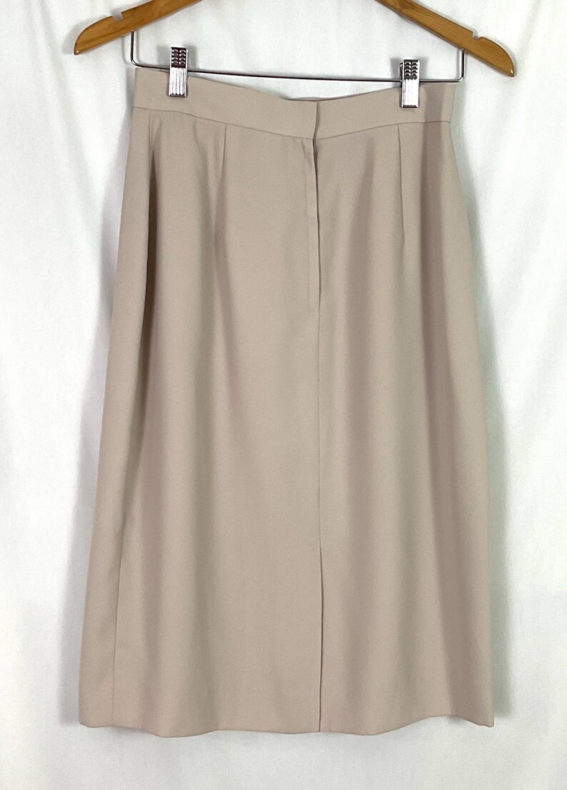 May include: A beige skirt with a back zipper closure. The skirt is knee-length and has a straight silhouette.