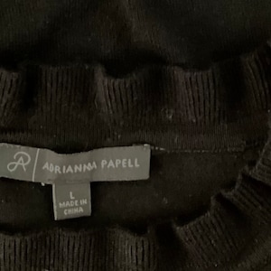 K&ouml;nnte beinhalten: Schwarzer Pullover mit R&uuml;schenkragen und einem Etikett mit der Aufschrift "Adrianna Papell" und "L" f&uuml;r die Gr&ouml;&szlig;e. Das Etikett tr&auml;gt au&szlig;erdem die Aufschrift "Made in China".