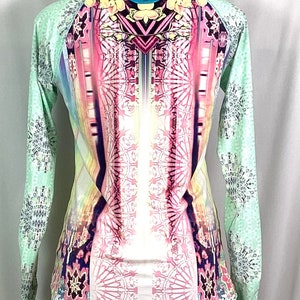 Op de afbeelding: Een shirt met lange mouwen met een kleurrijke, abstracte print. Het shirt is lichtgroen met een wit, roze en blauw ontwerp aan de voorkant en een wit, grijs en blauw ontwerp aan de mouwen.
