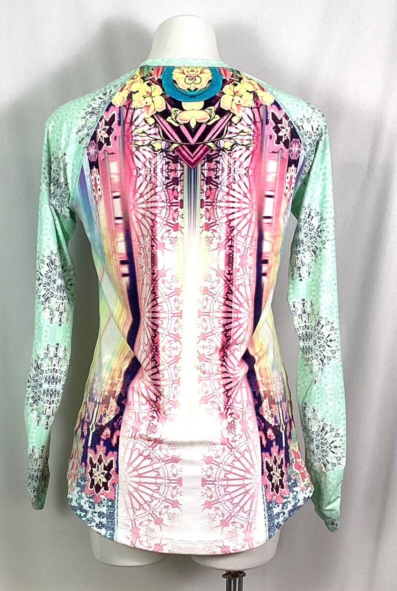 Op de afbeelding: Een shirt met lange mouwen met een kleurrijke, abstracte print. Het shirt is lichtgroen met een wit, roze en blauw ontwerp aan de voorkant en een wit, grijs en blauw ontwerp aan de mouwen.