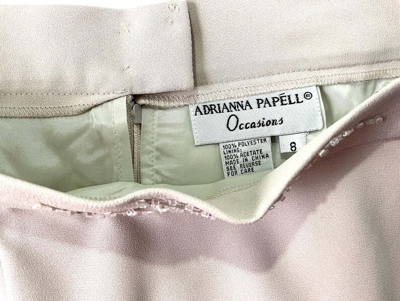 May include: A light pink skirt with a zipper closure and a label that reads "Adrianna Papell Occasions" with the details "100% Polyester, Lining: 100% Acetate, Made in China, See Reverse for Care" and the size "8".