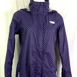 May include: A purple hooded jacket with white polka dots. The jacket has a zipper closure and two pockets. The North Face logo is visible on the left chest.