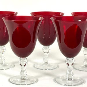 May include: Five ruby red wine glasses with clear stems and bases. The glasses have a tulip-shaped bowl and a classic design. The stem has a decorative, bulbous shape. The glasses are arranged in a group.