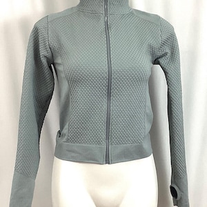 May include: A light gray zip-up jacket with a textured pattern. The jacket has a high collar and long sleeves.
