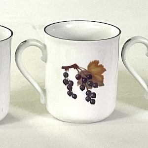 May include: Three white ceramic mugs with a dark rim and a handle on the side. Each mug features a botanical illustration of dark purple berries hanging from a brown stem with a single golden-brown leaf on the front surface of the vessel.