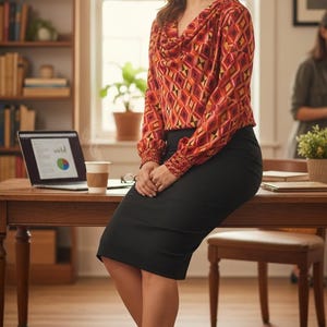 May include: A woman wearing a patterned blouse and a black pencil skirt, leaning on a wooden desk. She is wearing black high heels. A laptop and a coffee cup are on the desk.