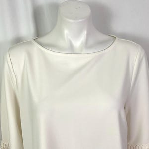 May include: A white, short-sleeved blouse with a round neckline and lace trim on the sleeves.