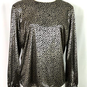 May include: A black long-sleeved blouse with a gold polka dot pattern. The blouse has a round neckline and long sleeves with gold trim.