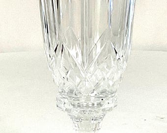 May include: A clear, cut-glass vase with a flared top and a pedestal base. The vase features vertical and diamond-shaped cut patterns, creating a textured and elegant appearance. Ideal for displaying flowers or as a decorative piece.
