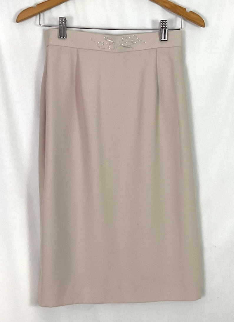 May include: A beige pencil skirt with a beaded floral design at the waistband.