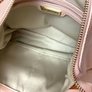 May include: Open view of a light pink handbag with a gold zipper and the brand name "VALENTINA" on a gold plate inside. The interior is a light beige color with a small pocket.