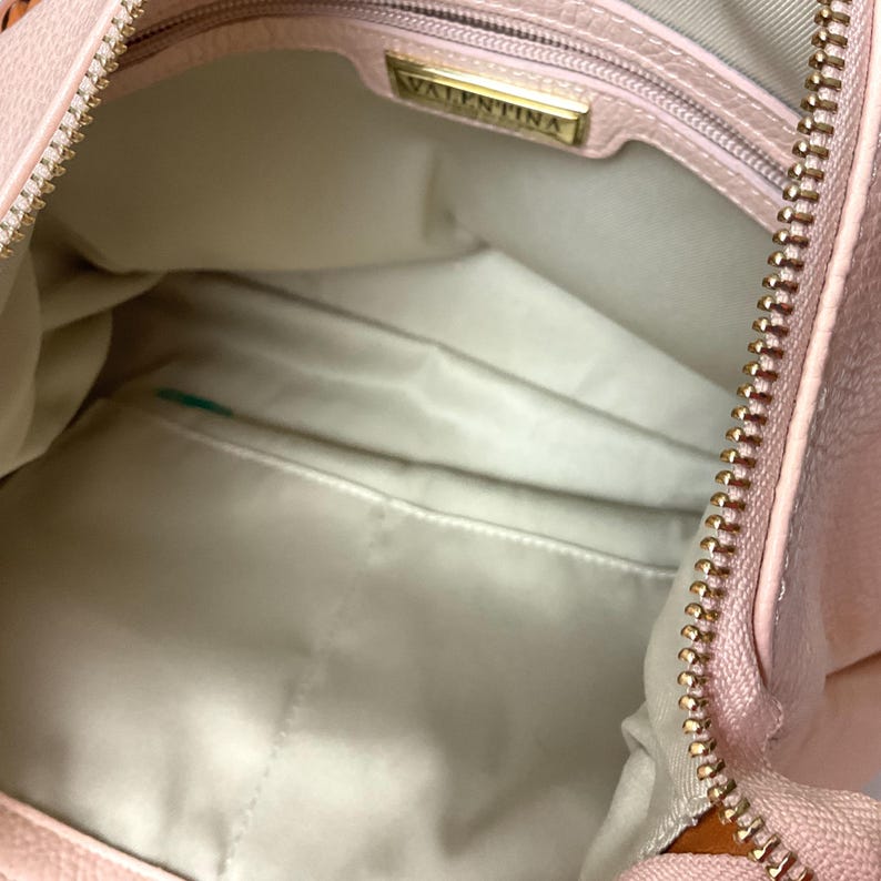 May include: Open view of a light pink handbag with a gold zipper and the brand name "VALENTINA" on a gold plate inside. The interior is a light beige color with a small pocket.