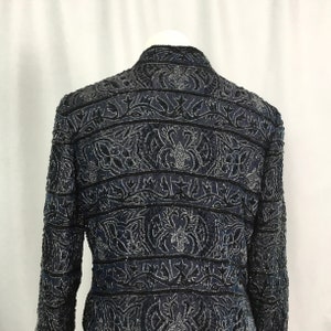 K&ouml;nnte beinhalten: Eine marineblaue Jacke mit aufwendigen Blumen- und Blattmustern, verziert mit silbernen und schwarzen Perlen. Die Jacke hat einen Stehkragen und lange &Auml;rmel. Die R&uuml;ckseite der Jacke zeigt die detaillierte Perlenarbeit und das Design.