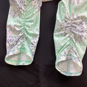 Op de afbeelding: Een paar groene en witte leggings met een patroon en een geplooide detail aan de onderkant van elk been.