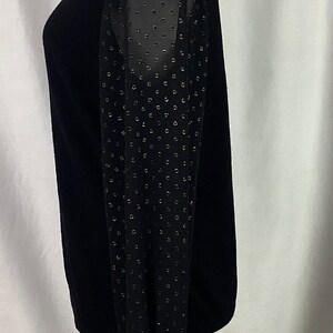 K&ouml;nnte beinhalten: Schwarzer Pullover mit langen &Auml;rmeln. Die &Auml;rmel sind aus durchsichtigem Stoff mit schwarzem Punktmuster.