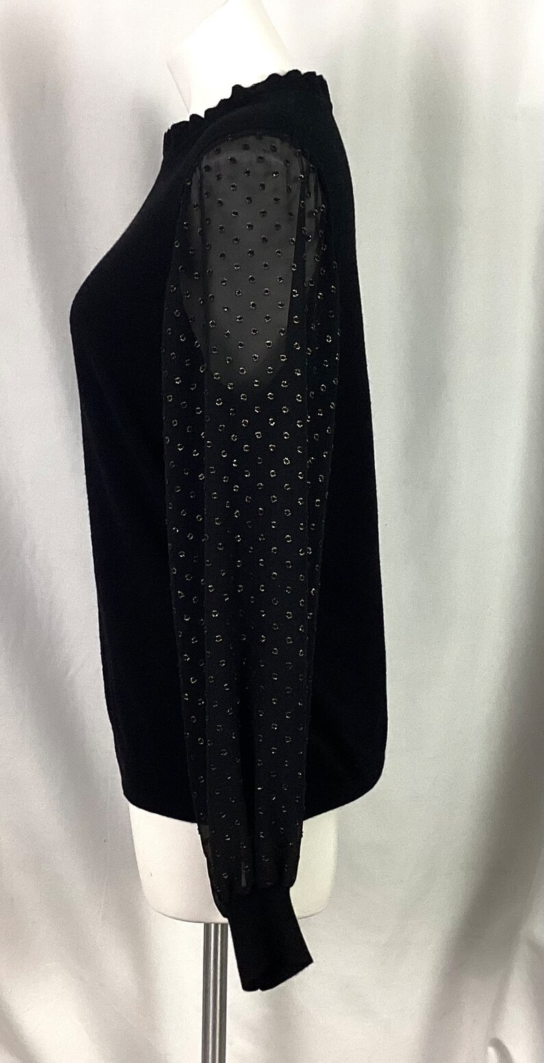 K&ouml;nnte beinhalten: Schwarzer Pullover mit langen &Auml;rmeln. Die &Auml;rmel sind aus durchsichtigem Stoff mit schwarzem Punktmuster.