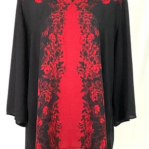 May include: Black V-neck blouse with a striking red floral design. The blouse features long sleeves and a central panel of red fabric, adorned with a symmetrical pattern of red flowers and leaves. The overall design is elegant and eye-catching.