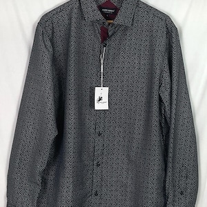 May include: A long-sleeved button-down shirt with a black and white polka dot pattern. The shirt has a burgundy collar lining and a hang tag with a logo. The shirt is displayed on a wooden hanger.