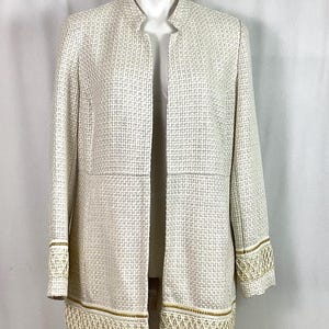 May include: A white open-front jacket with a gold trim and a woven pattern. The jacket has a mandarin collar and long sleeves.