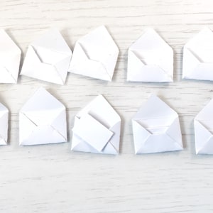Peut inclure: Dix petites enveloppes en papier blanc dispos&eacute;es sur une surface en bois clair. Une enveloppe contient une petite carte rectangulaire blanche. Les enveloppes sont ouvertes, pr&ecirc;tes &agrave; &ecirc;tre utilis&eacute;es.