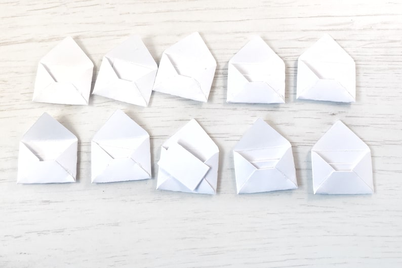 Peut inclure: Dix petites enveloppes en papier blanc dispos&eacute;es sur une surface en bois clair. Une enveloppe contient une petite carte rectangulaire blanche. Les enveloppes sont ouvertes, pr&ecirc;tes &agrave; &ecirc;tre utilis&eacute;es.