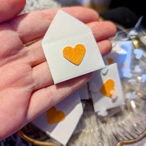 Peut inclure: Petites enveloppes en papier blanc avec un c&oelig;ur orange scintillant. Plusieurs enveloppes sont visibles, certaines nettes, d'autres floues. Les enveloppes sont dispos&eacute;es dans un plat d&eacute;coratif transparent.