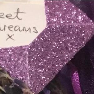 Peut inclure: Gros plan sur un objet d&eacute;coratif avec un n&oelig;ud violet scintillant et une petite &eacute;tiquette blanche. L'&eacute;tiquette porte les mots manuscrits "sweet dreams x". L'arri&egrave;re-plan comprend de la lavande s&eacute;ch&eacute;e et du tissu violet fonc&eacute;.