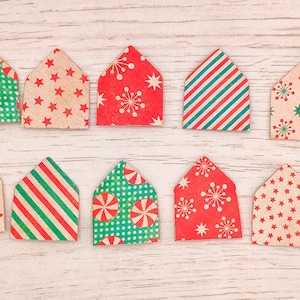 May include: Ten house-shaped decorations with festive patterns. Designs include red and white peppermint candies, red stars, green polka dots, red and green stripes, and white snowflakes. The ornaments are arranged on a light wood-grain surface.