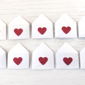 Peut inclure: Dix enveloppes en papier blanc, chacune orn&eacute;e d'un c&oelig;ur rouge paillet&eacute; sur le devant. Les enveloppes sont dispos&eacute;es en deux rang&eacute;es de cinq, sur un fond de grain de bois blanc. Les c&oelig;urs ajoutent une touche d'&eacute;clat.
