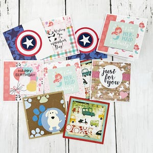 May include: A collection of handmade greeting cards with various designs. Some cards feature Captain America shields, mermaids, and birthday themes. Others have text that reads "Wishing You a Upandous Day!", "Happy Birthday", and "Just for You".