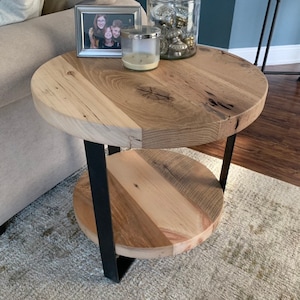 May include: A round wooden end table with a black metal frame and two shelves. The table has a rustic, reclaimed wood look and is decorated with a picture frame and a candle.