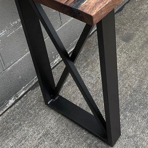 May include: Close-up of a black metal table leg with a geometric design. The leg is made of thick, sturdy metal and has a matte black finish.