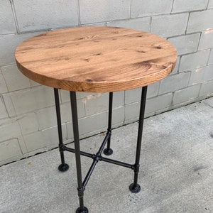 May include: A round wooden table top with a natural wood finish sits on a black metal pipe base. The table has a simple, industrial design.