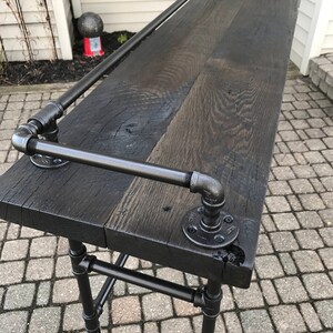 May include: A black wooden bar top with a black metal pipe frame and a black metal handrail. The bar top is made of reclaimed wood and has a rustic look.