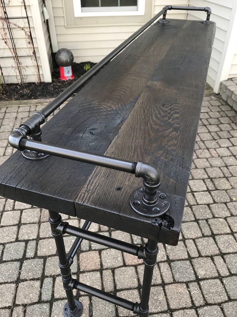 May include: A black wooden bar top with a black metal pipe frame and a black metal handrail. The bar top is made of reclaimed wood and has a rustic look.