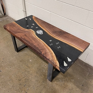 May include: A walnut wood coffee table with a black epoxy river and a Star Wars Millennium Falcon inlay. The table has black metal legs.