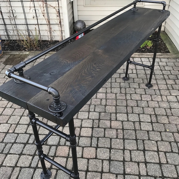 May include: A black wooden bar table with a black metal pipe frame and a black metal handrail. The table is sitting on a gray brick patio.