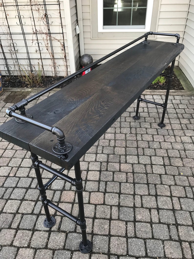 May include: A black wooden bar table with a black metal pipe frame and a black metal handrail. The table is sitting on a gray brick patio.