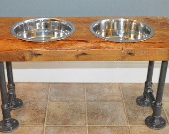 May include: A wooden dog bowl stand with two stainless steel bowls. The stand is made of reclaimed wood and has a rustic look. The legs are made of black metal pipe.