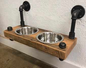 May include: A rustic wooden dog bowl stand with two stainless steel bowls. The stand is mounted to the wall with black industrial pipe brackets.