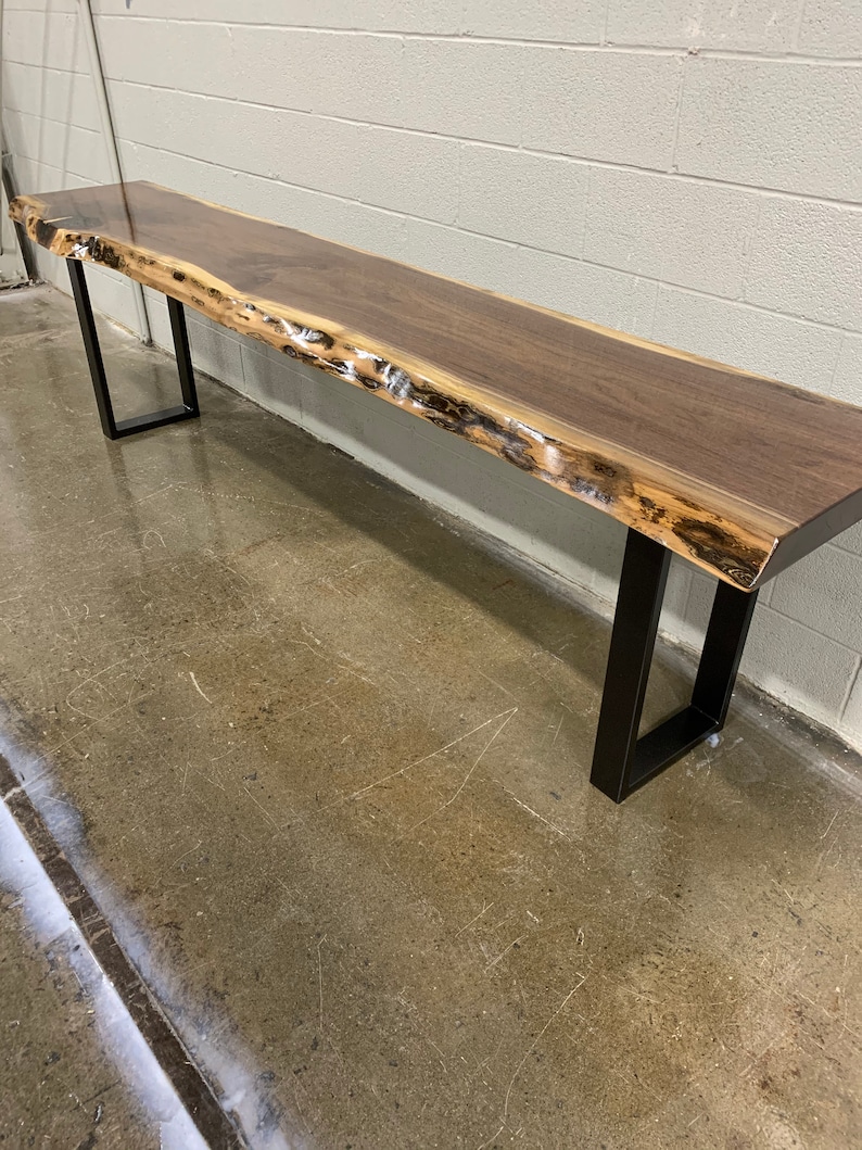 May include: A long, live edge walnut wood table with a natural, live edge finish. The table is supported by two black metal legs.