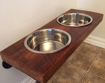 May include: A wooden dog bowl stand with two stainless steel bowls. The stand is mounted to the wall with metal brackets.