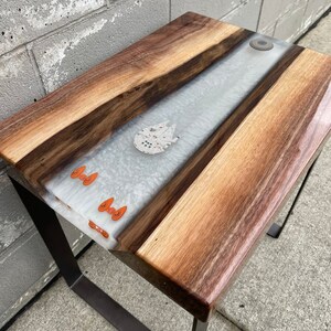 May include: A wooden end table with a white epoxy river and a small spaceship figurine. The table has a black metal frame.