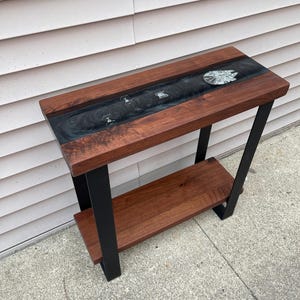 May include: A rectangular console table featuring two tiers of dark brown wood with a central river of black epoxy resin. The resin inlay contains embedded miniature starship models, including a circular spacecraft and several smaller fighter ships.