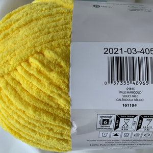 Puede incluir: Una madeja de hilo amarillo super grueso, etiquetada como "Pale Marigold" con el c&oacute;digo de producto "2021-03-405". El hilo es 100% poli&eacute;ster y se puede lavar y secar a m&aacute;quina.