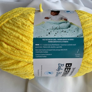 Puede incluir: Una madeja de hilo amarillo Bernat Baby Blanket con una etiqueta que dice "Free Pattern on Label/Patron Gratuit au Verso/Patron Gratuito en la Etiqueta" e incluye instrucciones para tejer una manta de beb&eacute; con motivo de granny. La etiqueta tambi&eacute;n dice "Crochet Granny Motif Blanket/Couverture crochet&eacute;e motif grand-m&egrave;re/Manta estilo abuelita a ganchille".